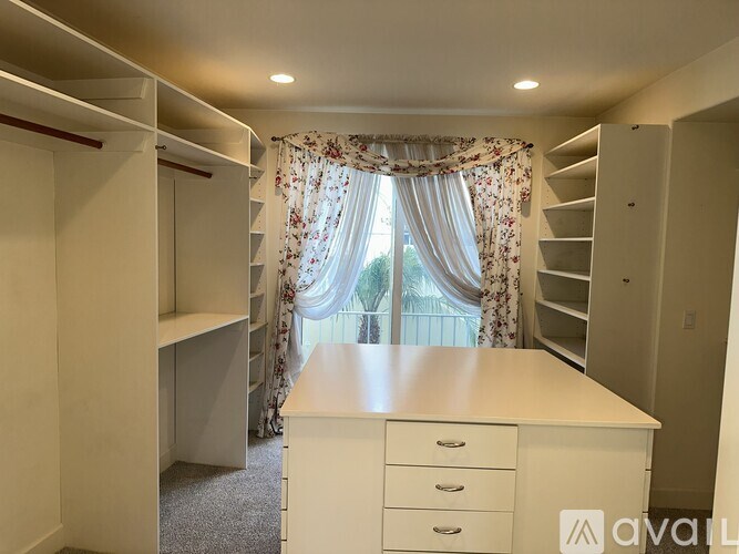 A white desk with drawers is in a room with a window and curtains.
