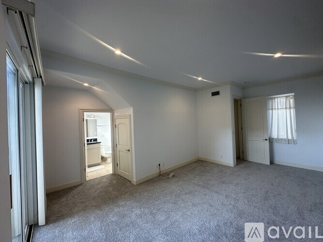 A spacious room with a carpeted floor and a window with curtains.