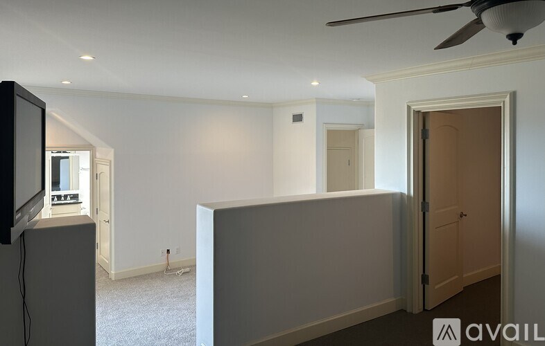 A room with a ceiling fan and a flat screen TV mounted on the wall.