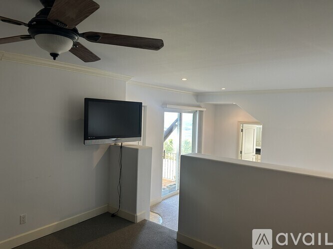 A room with a ceiling fan and a television mounted on the wall.