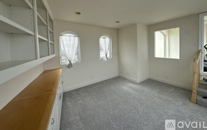A room with a carpeted floor, a wooden counter, and three windows.