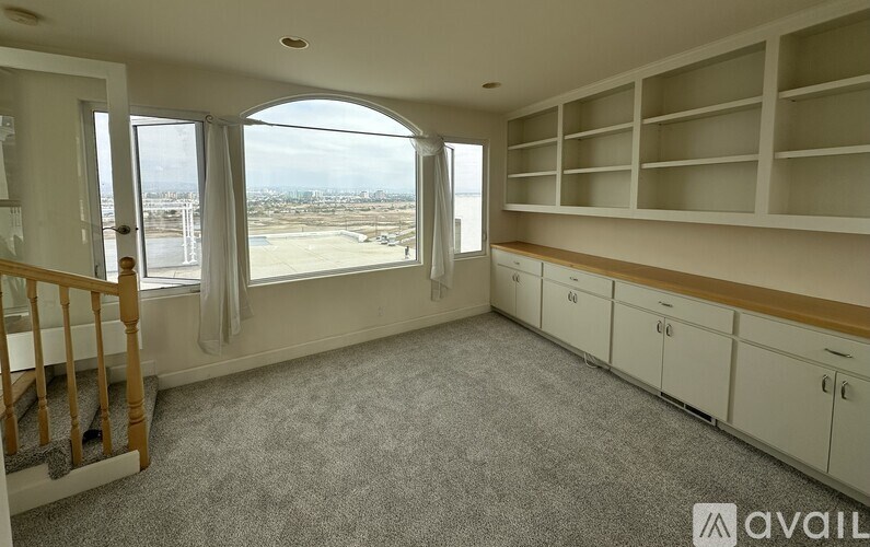 A room with a carpeted floor, a staircase, and a view of the outside through a large window.