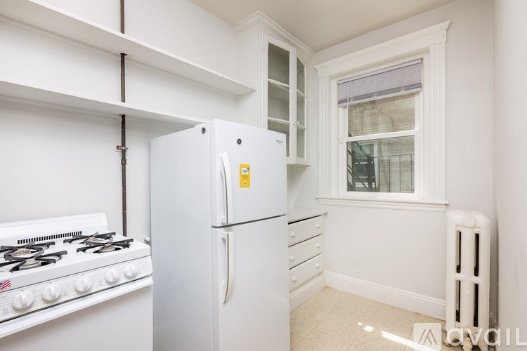 A white kitchen with a fridge, stove and a window.