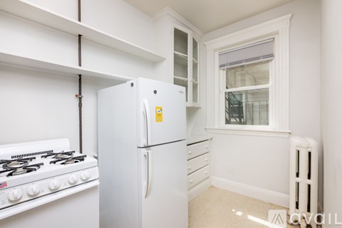 A white kitchen with a fridge, stove and a window.