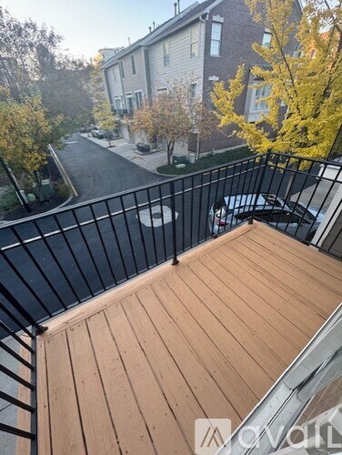 A balcony with a black railing and wooden flooring overlooks a street with houses and trees.