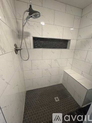 A bathroom with a marble tile shower and a black and white tiled floor.