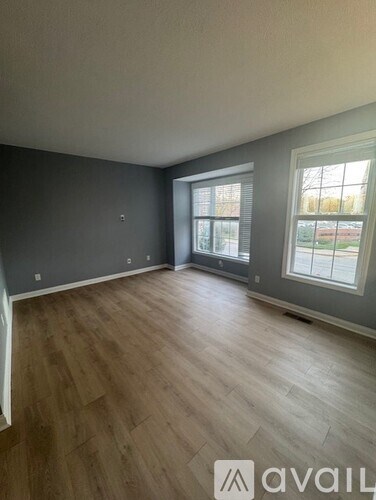 A room with wooden flooring and two windows.