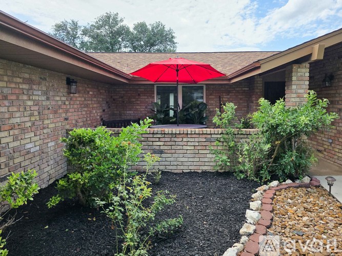 A red umbrella is on a patio with a brick wall and a landscaped garden.