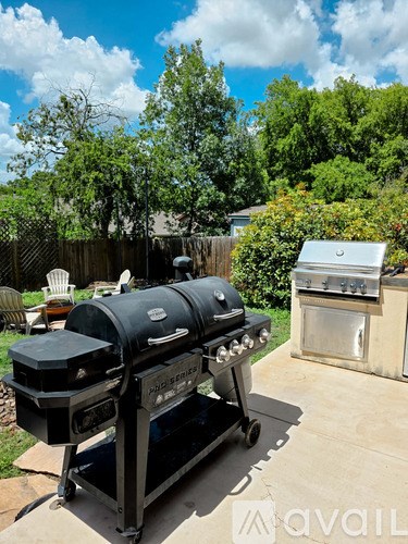 A black barbecue grill with a silver lid is in the foreground of a sunny backyard.