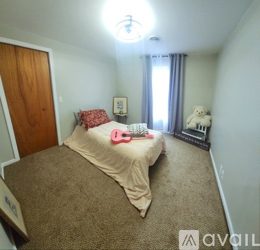 A bedroom with a bed, a teddy bear, and a pink guitar.