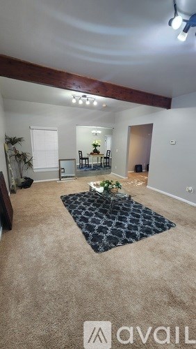 A living room with a rug, chairs, and a table with a vase of flowers on it.