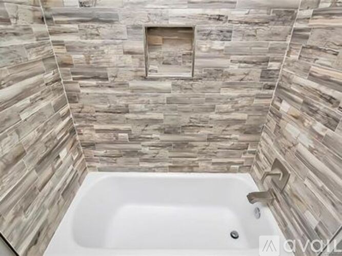 A white bathtub sits in a bathroom with a stone wall.