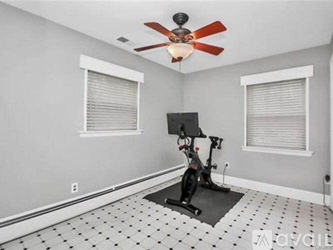 A room with a fan, exercise bike, and windows.
