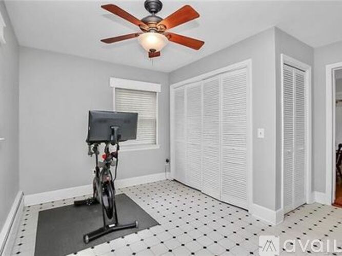 A room with a ceiling fan and a stationary exercise bike on the floor.