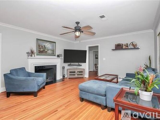 A living room with a fireplace, a blue chair, a blue ottoman, a coffee table, a ceiling fan, and a painting on the wall.