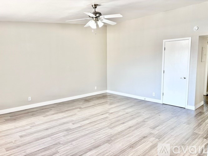 A room with a ceiling fan and light fixture, wooden flooring, and a white door.
