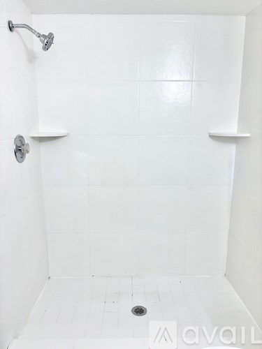 A white tiled shower with a drain in the middle.