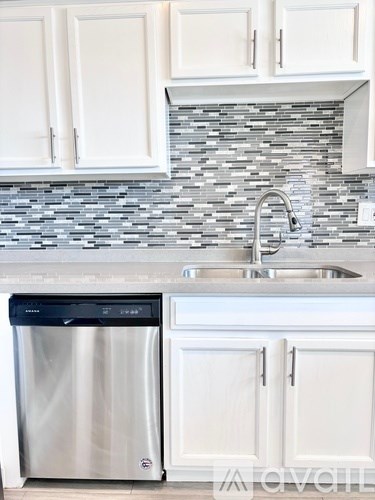 A kitchen with a stainless steel dishwasher and white cabinets.