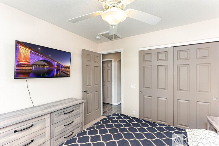 A bedroom with a television, a bed, and a ceiling fan.