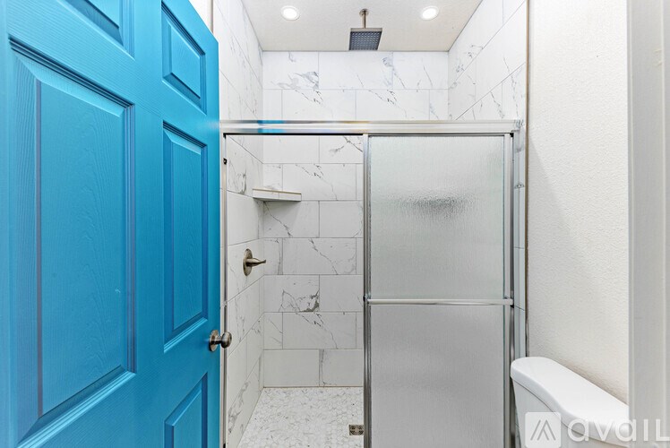 A blue door is on the left of a white tiled shower.