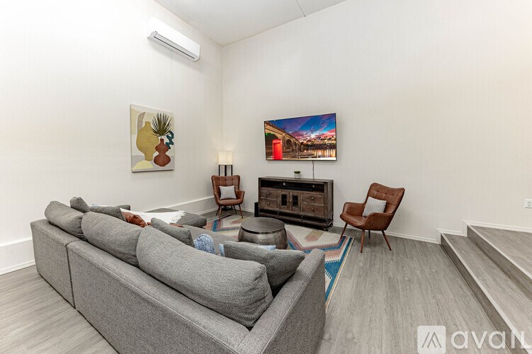 A living room with a grey sofa, a wooden chair, and a painting of a pineapple and a pineapple on the wall.