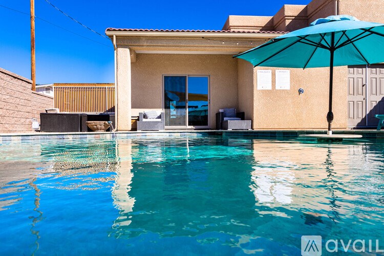 A pool in front of a house with a blue umbrella.