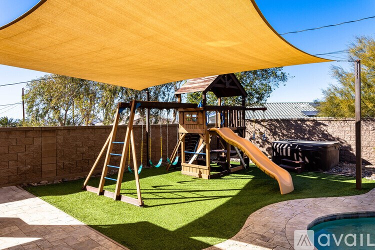 A playground with a yellow shade sail over a wooden swing set.