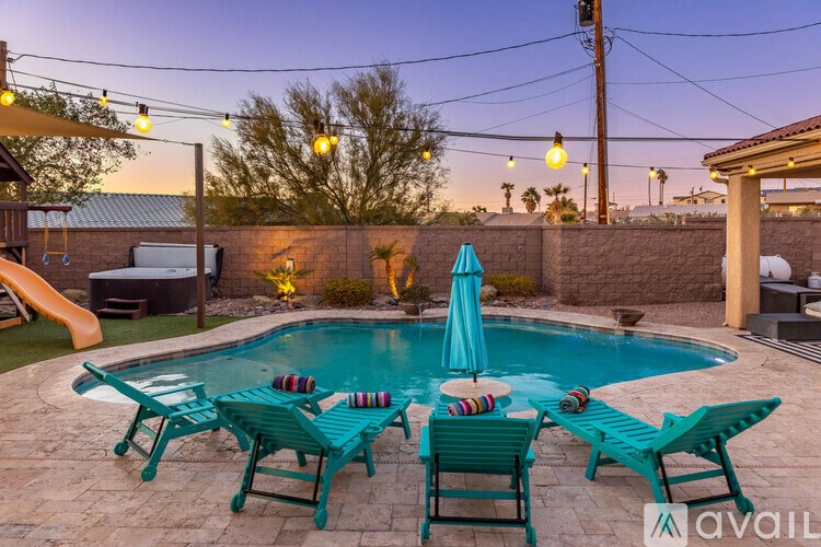 A pool surrounded by chairs and umbrellas with a sunset in the background.