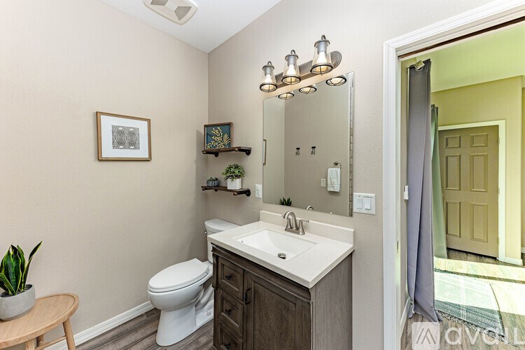 A bathroom with a toilet, sink, mirror, and a plant.