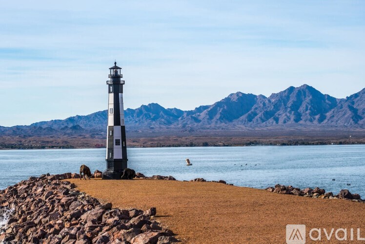 A lighthouse stands on a rocky shore with mountains in the background.
