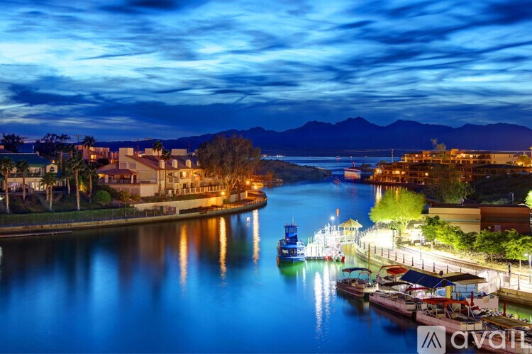 A serene night view of a river with boats docked on the right and a mountain range in the distance.