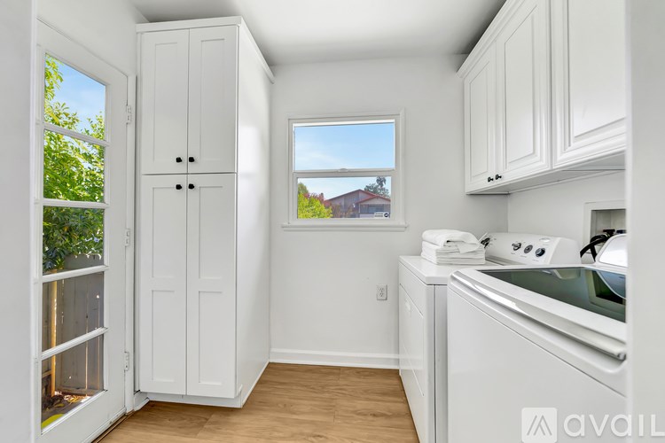 A kitchen with white cabinets and a window overlooking a red house.
