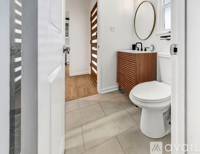 A white toilet in a bathroom with a wooden cabinet and a round mirror above it.