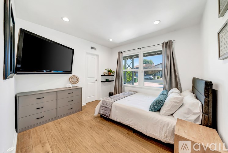 A bedroom with a large bed, a television, and a window with curtains.