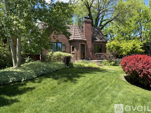 A house with a red brick exterior and a chimney is surrounded by a well-manicured lawn and trees.