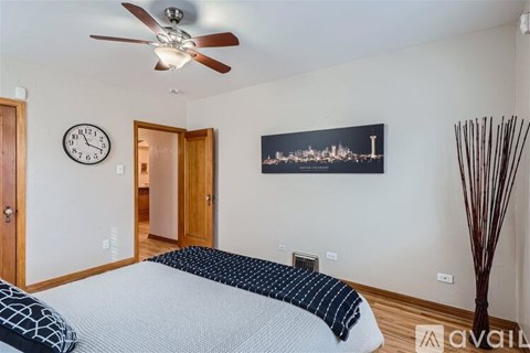 A bedroom with a bed, a ceiling fan, a clock, and a picture of a city skyline.