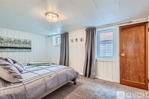 A bedroom with a bed, a window with curtains, and a wooden door.