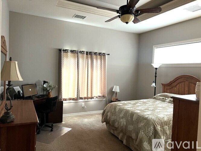 A bedroom with a bed, desk, and window with curtains.