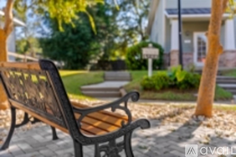 A bench with a black frame and a wooden slat back sits on a brick walkway.