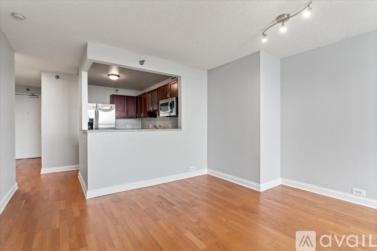 A room with wooden floors and white walls, with a kitchen area visible in the background.