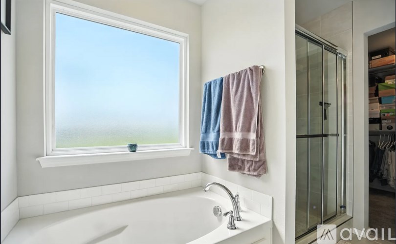 A white bathtub with a window above it and towels hanging on the wall.