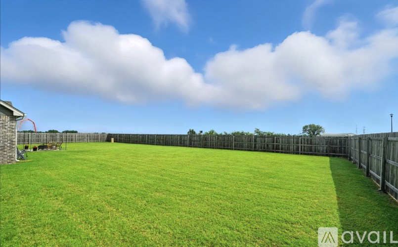 A large, open grassy field with a fence and a small building in the background.