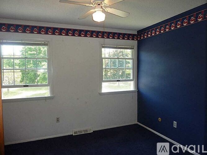 A room with a ceiling fan and two windows.