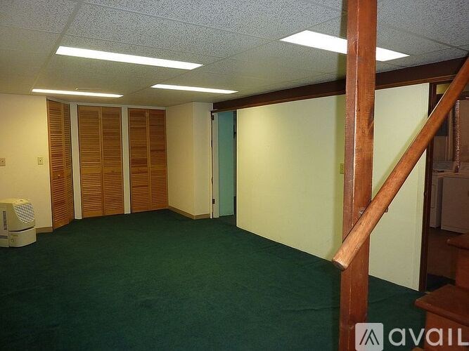 A room with green carpet and wooden staircase.