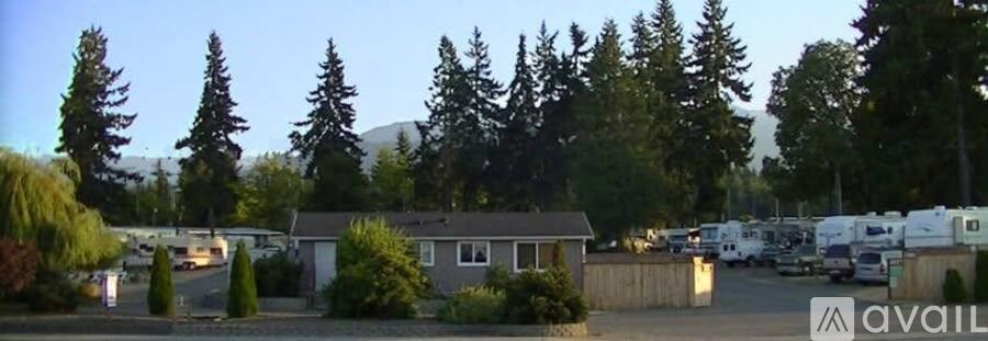A small house is surrounded by trees and a parking lot.