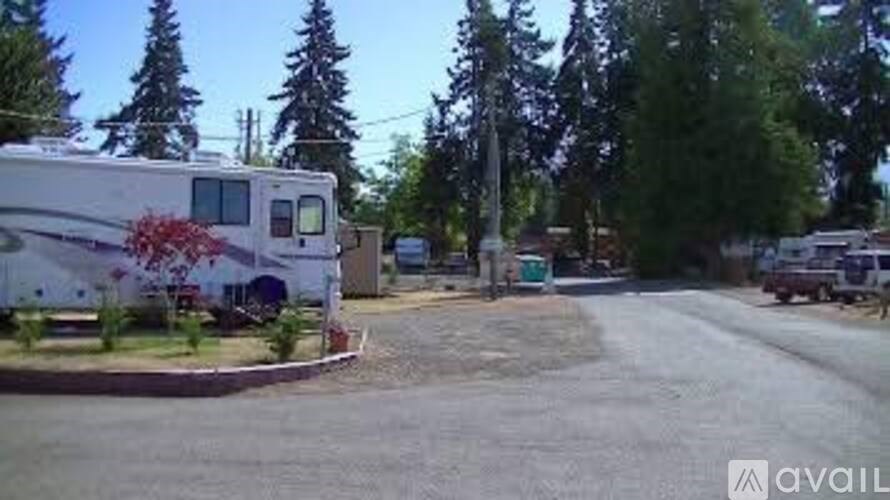 A white RV is parked in a lot with trees in the background.