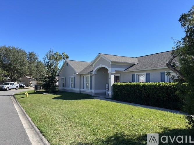 A house with a white exterior and a grey roof is surrounded by a green lawn and trees.