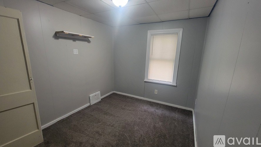 A room with a carpeted floor, a window with blinds, and a light fixture on the ceiling.