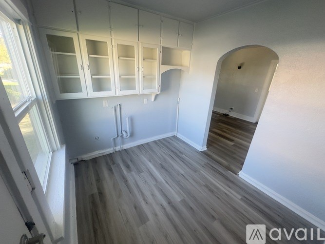 A room with white walls and wooden flooring, featuring a set of stairs and a large archway.