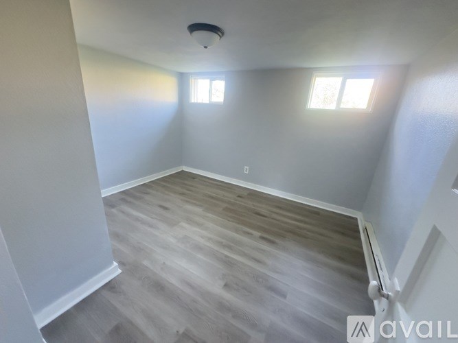 A room with wooden flooring and two windows.